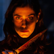 A woman, in shadow except for light across her face, holds a bloody knife in a scene from The Advent Calendar.